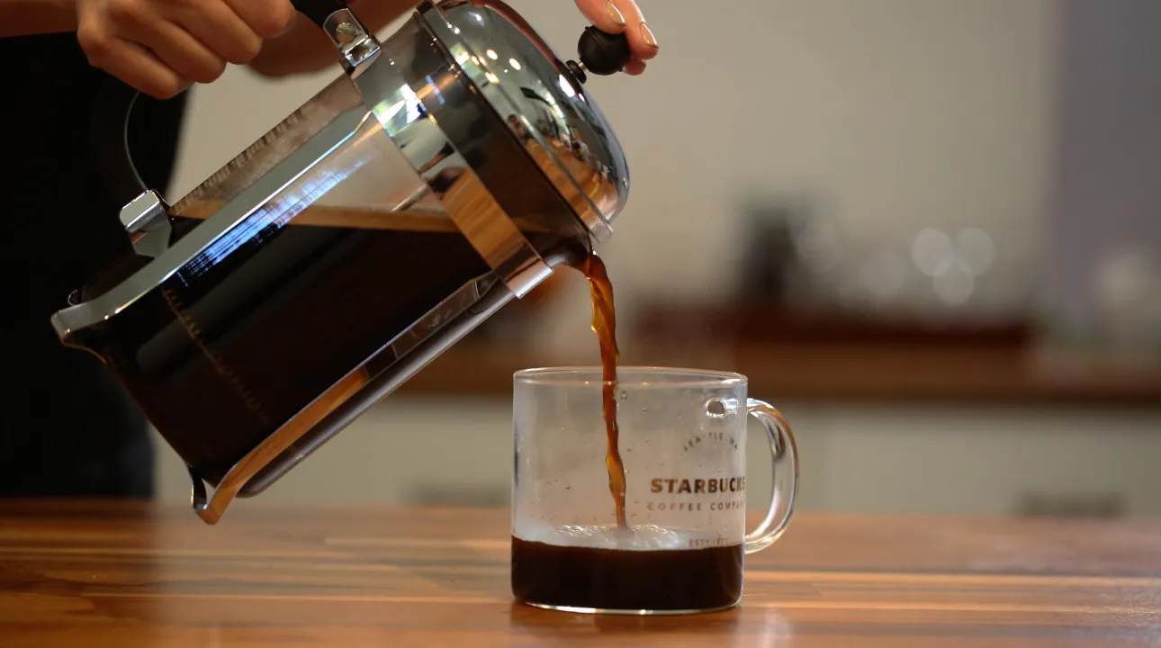 Pouring coffee out of a coffee press into glass coffee mug 